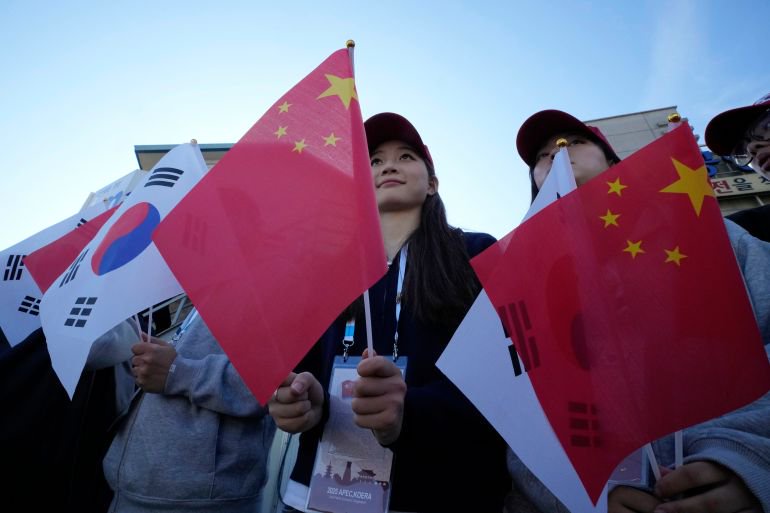 People wave Chinese flags as they wait for arrival of China's President Xi Jinping as he attends the Asia-Pacific Economic Cooperation outside of Gimhae International Airport in Busan South Korea, Thursday, Oct. 30, 2025. (AP Photo/Ahn Young-joon)