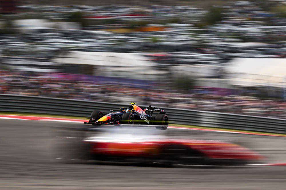 Red Bull F1 car racing on track at the United States Grand Prix, blurred crowd and grandstands behind, Isack Hadjar's race