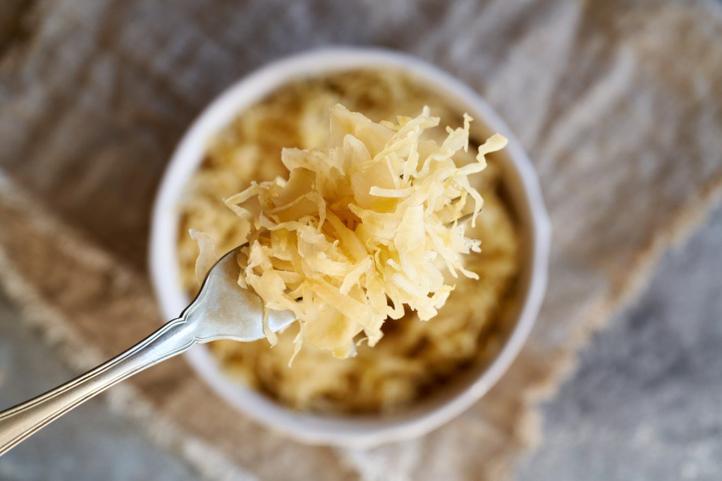 Homemade fermented cabbage or sauerkraut on a fork above a bowl, top view.