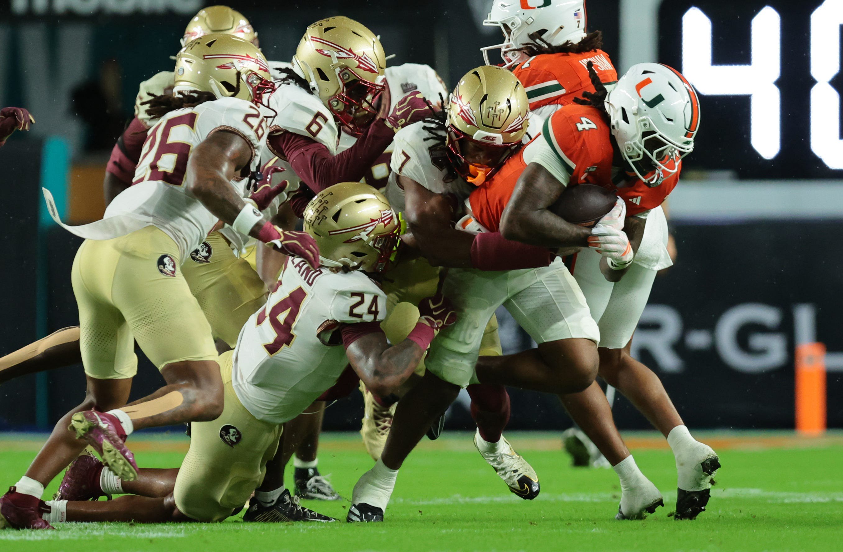 Oct 17, 2026; Miami Gardens, Florida, USA;  Miami Hurricanes running back Mark Fletcher Jr. (4) is tackled by Florida State Seminoles defensive back Ashlynd Barker (7) and defensive back K.J. Kirkland (24) during the second quarter at Hard Rock Stadium.  Mandatory Credit: Sam Navarro-Imagn Images