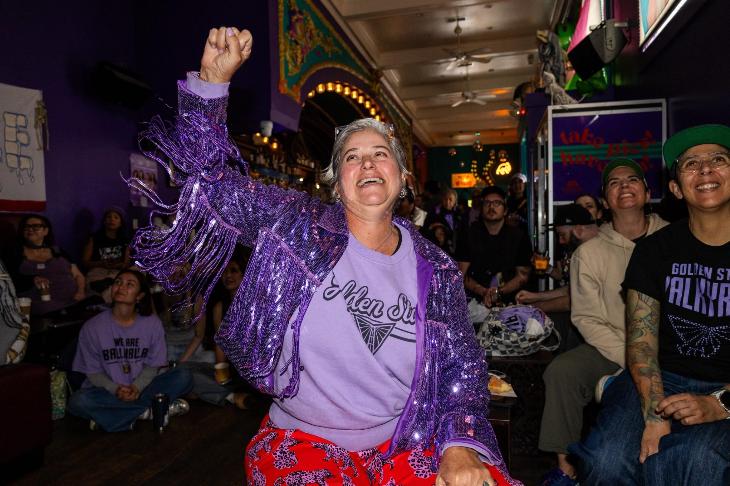 A woman with a purple sequin fringe jacket raises her fist in a crowd.