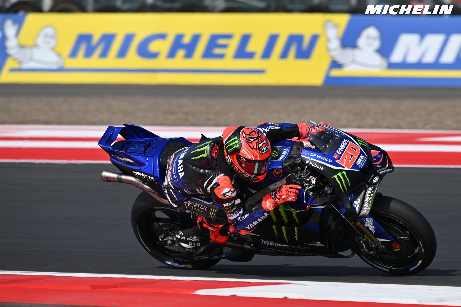 Fabio Quartararo on his Yamaha M1 leaning into a corner at a MotoGP race, wearing Monster Energy and Yamaha blue-and-red leathers, #20 bike.