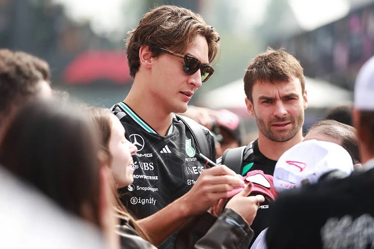 Driver in black Mercedes-AMG Petronas-style team kit signing autographs for fans in a paddock crowd at an F1 event