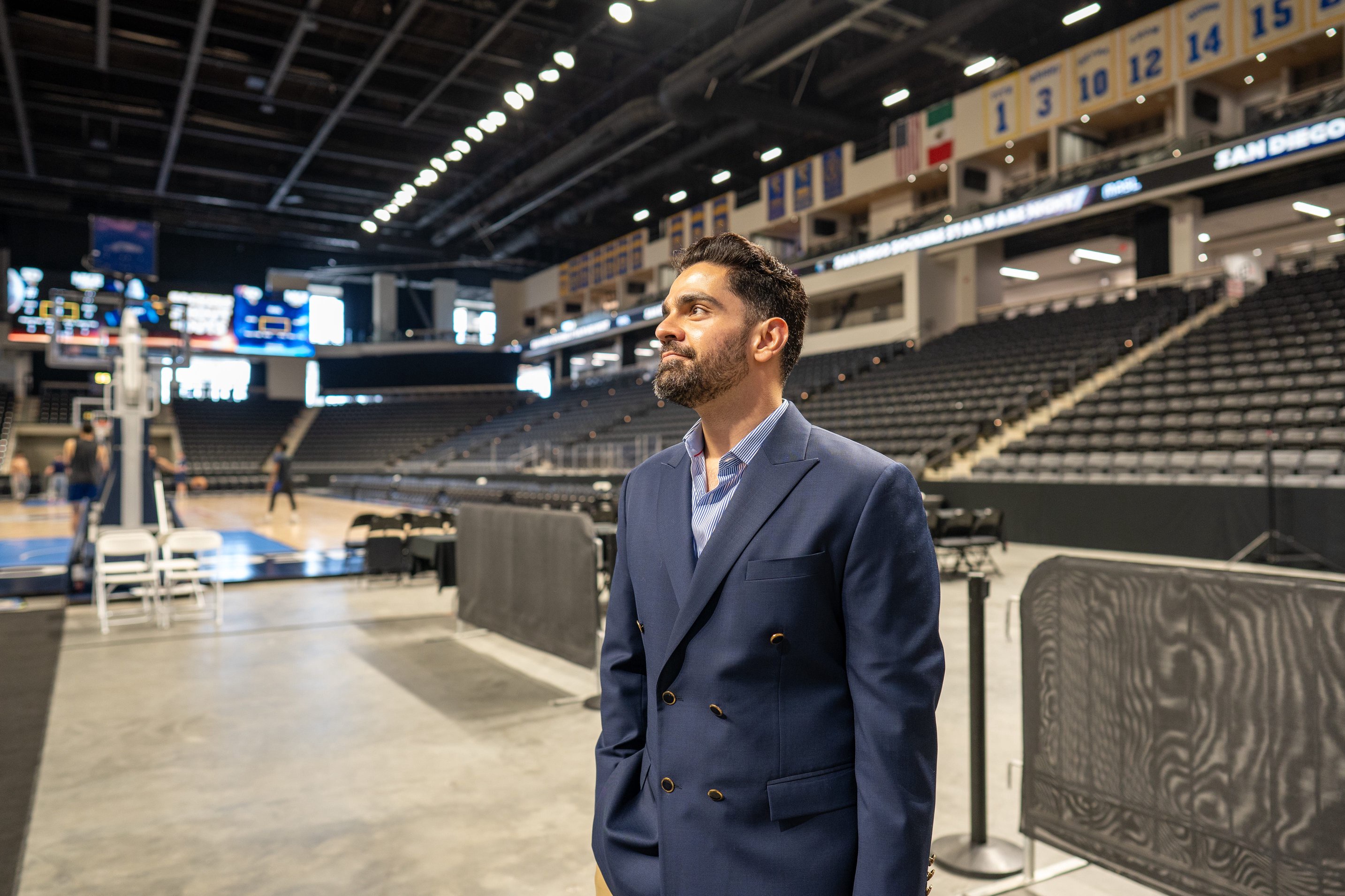Hardik Jagda is standing inside a sports stadium wearing a dark navy suit.