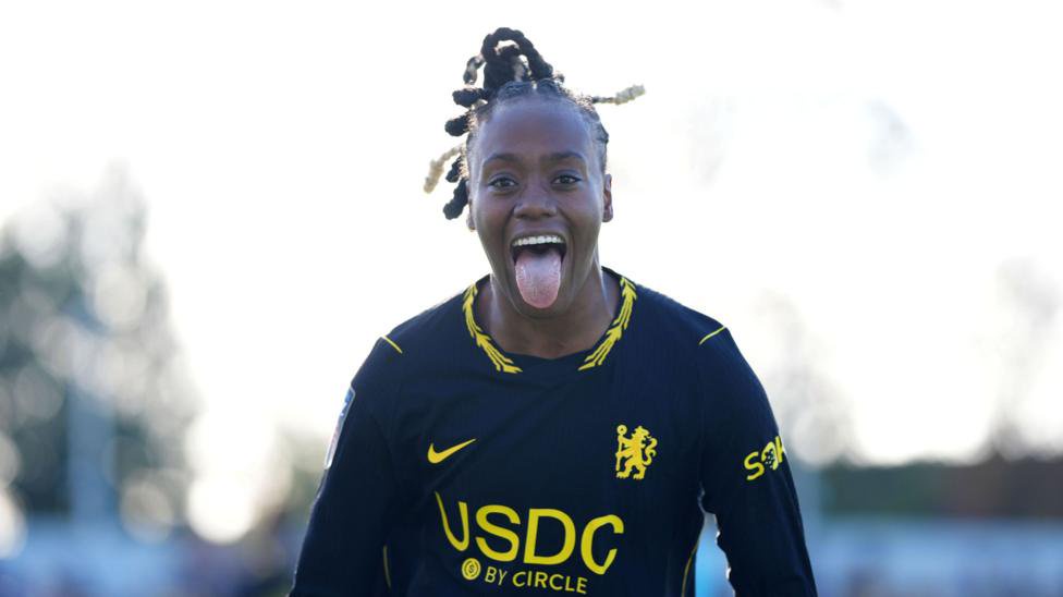 Melvine Malard, wearing a black kit with yellow details, with her tongue out
