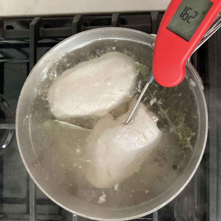 cooked chicken in a pot of liquid with a thermometer reading the temperature