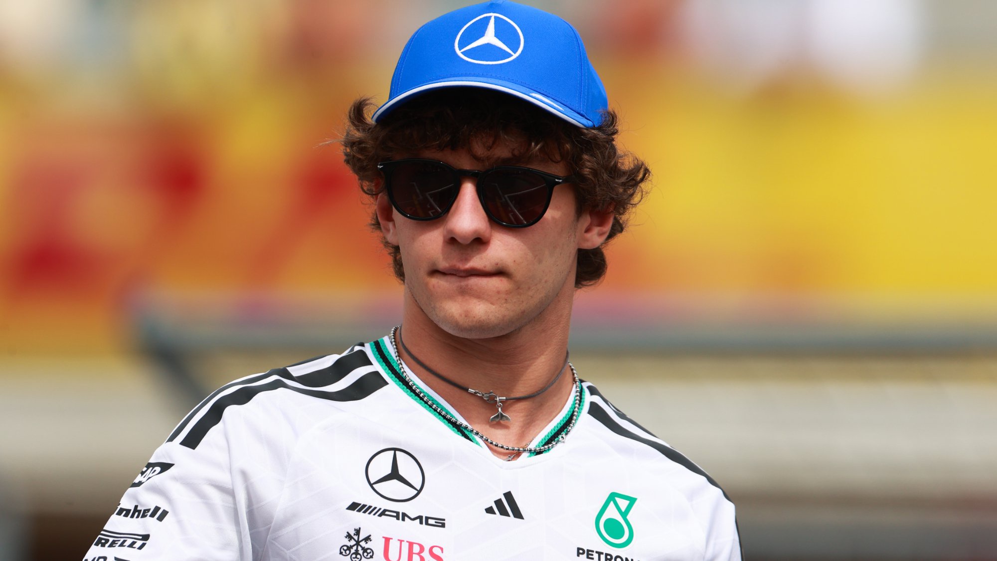 F1 driver Kimi Antonelli looking onwards, wearing a cap and sunglasses.