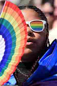 A marcher donning rainbow sunglasses and holding a rainbow fan