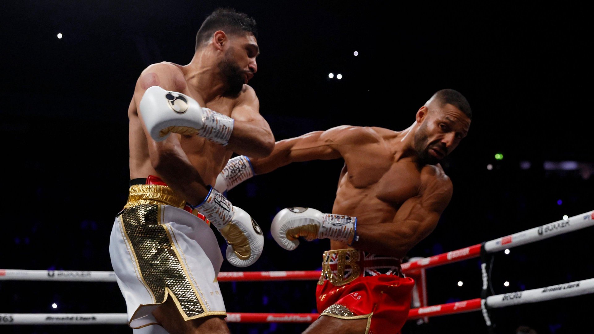 Amir Khan (left) and Kell Brook (right) exchange punches during a professional boxing match. Khan, wearing white and gold shorts and white boxing gloves.