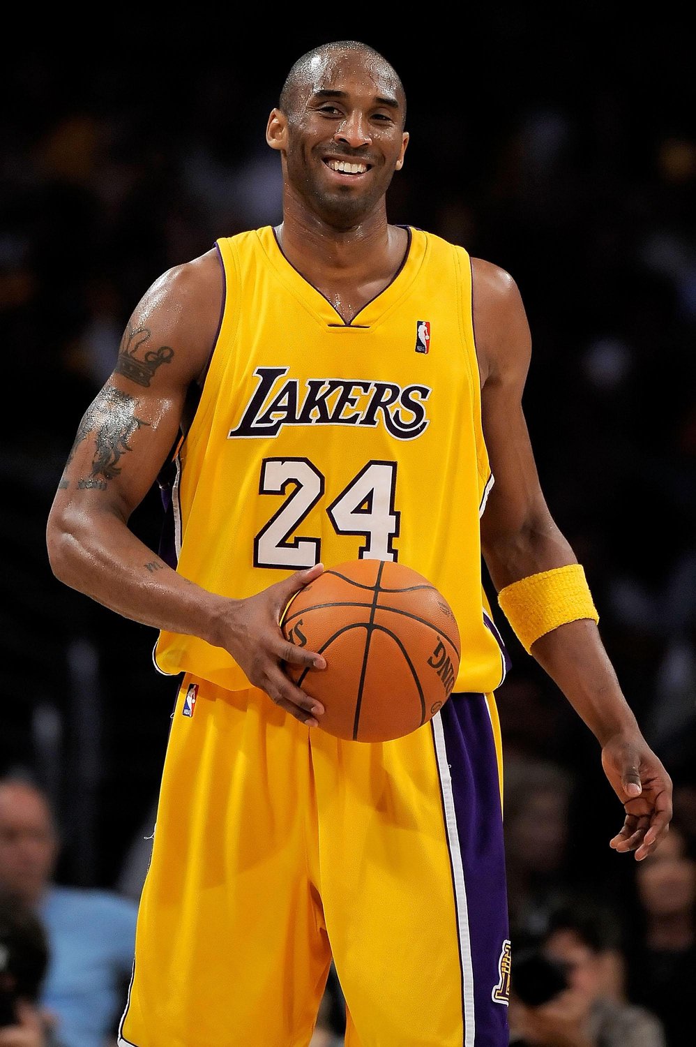 Kobe Bryant in a Los Angeles Lakers jersey holding a basketball and smiling.