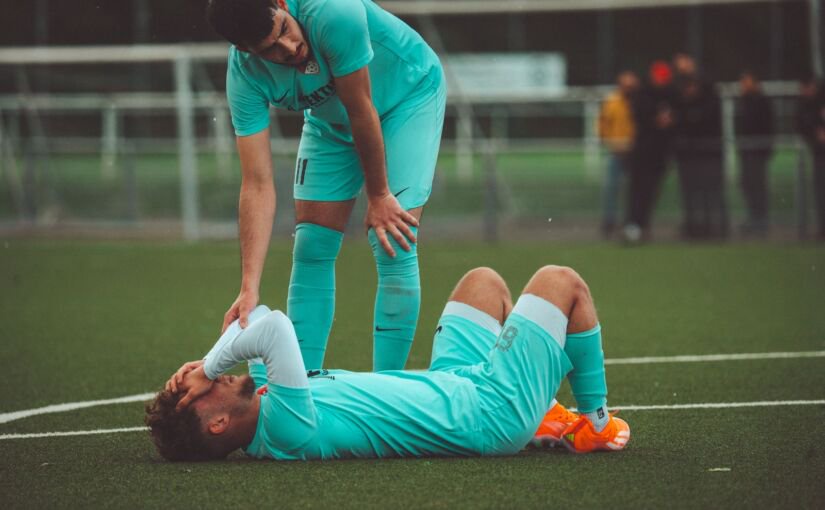 Injured footballer lying on the pitch as a teammate checks on him