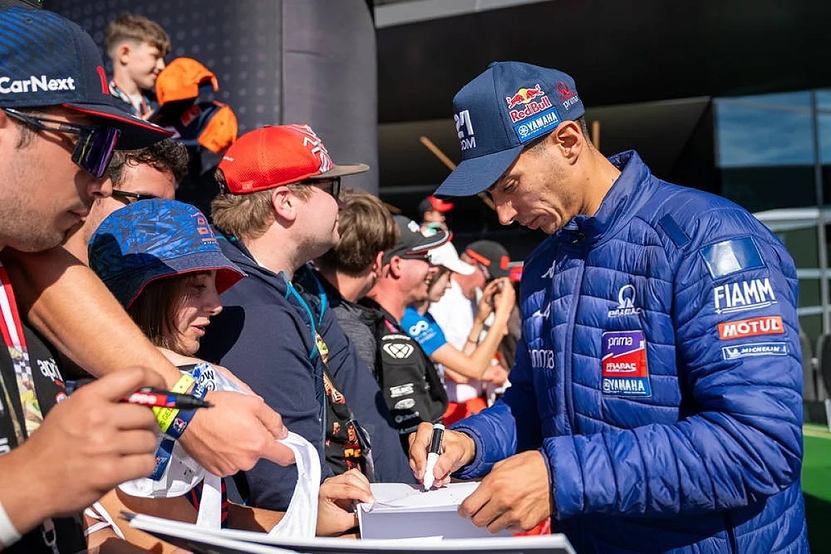 A rider in a navy Yamaha MotoGP jacket and cap signs autographs for fans in the paddock, with Fiamm, Motul and Michelin logos visible.