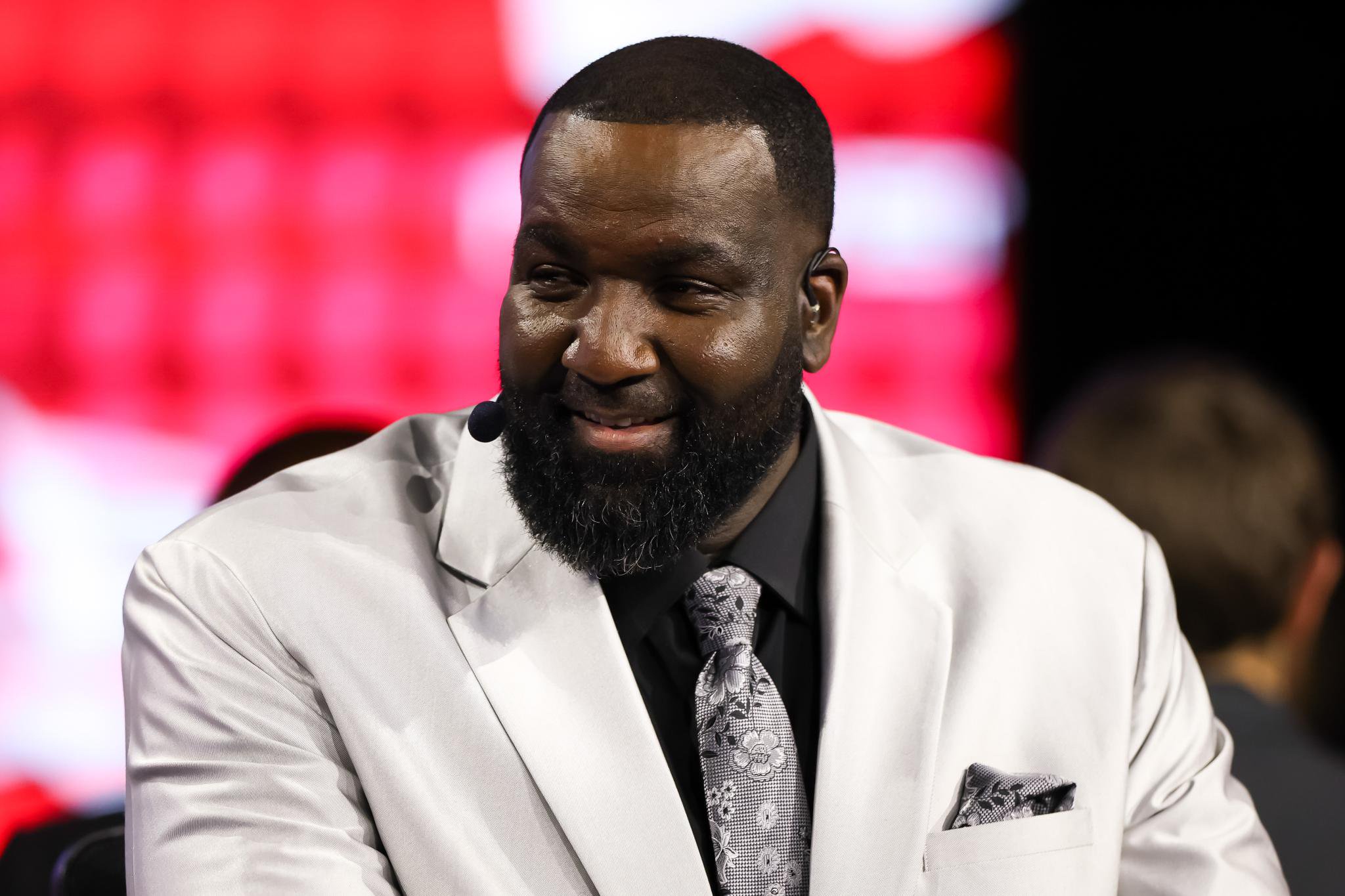 Kendrick Perkins smiling while wearing a white suit jacket and patterned tie.