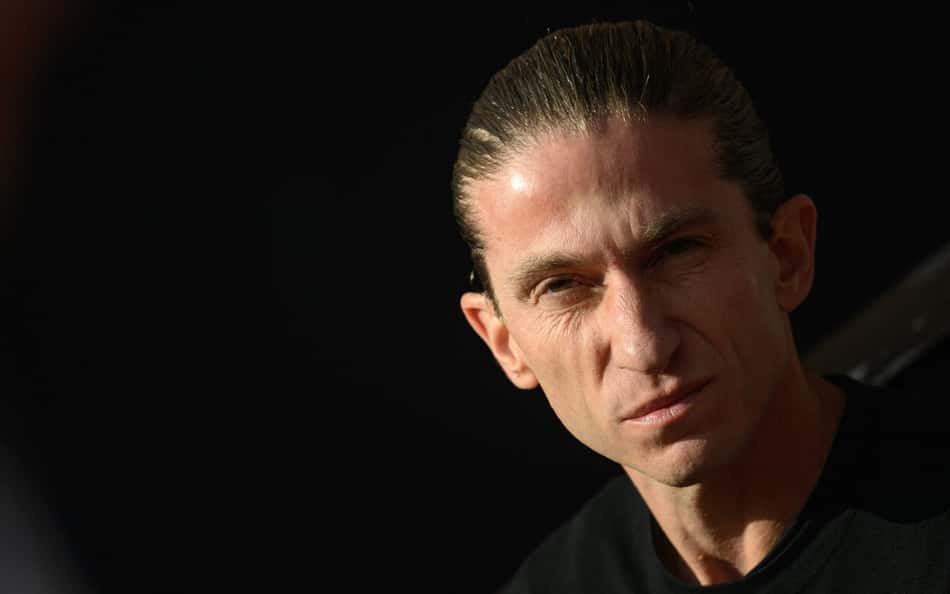 Retrato de homem com cabelo puxado para trás, expressão séria, camiseta preta.