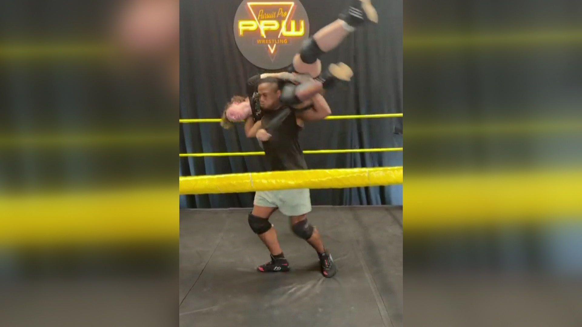 A wrestler lifts his opponent up inside a wrestling ring.