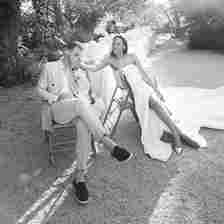 Black and White Image of Bride in Wedding Dress Sitting With Groom in Suit at Outdoor Reception