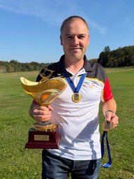 Ein Mann hält einen Pokal und eine Medaille in der Hand