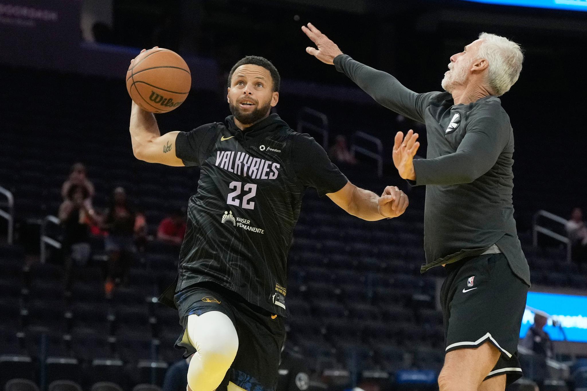 Golden State Warriors guard Stephen Curry warms up with assistant coach Bruce Fraser, wearing a Golden State Valkyries Veronica Burton jersey.