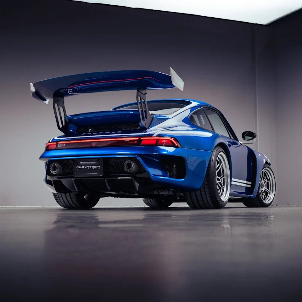 A sleek blue sports car with a large rear wing, showcased in a modern indoor setting.