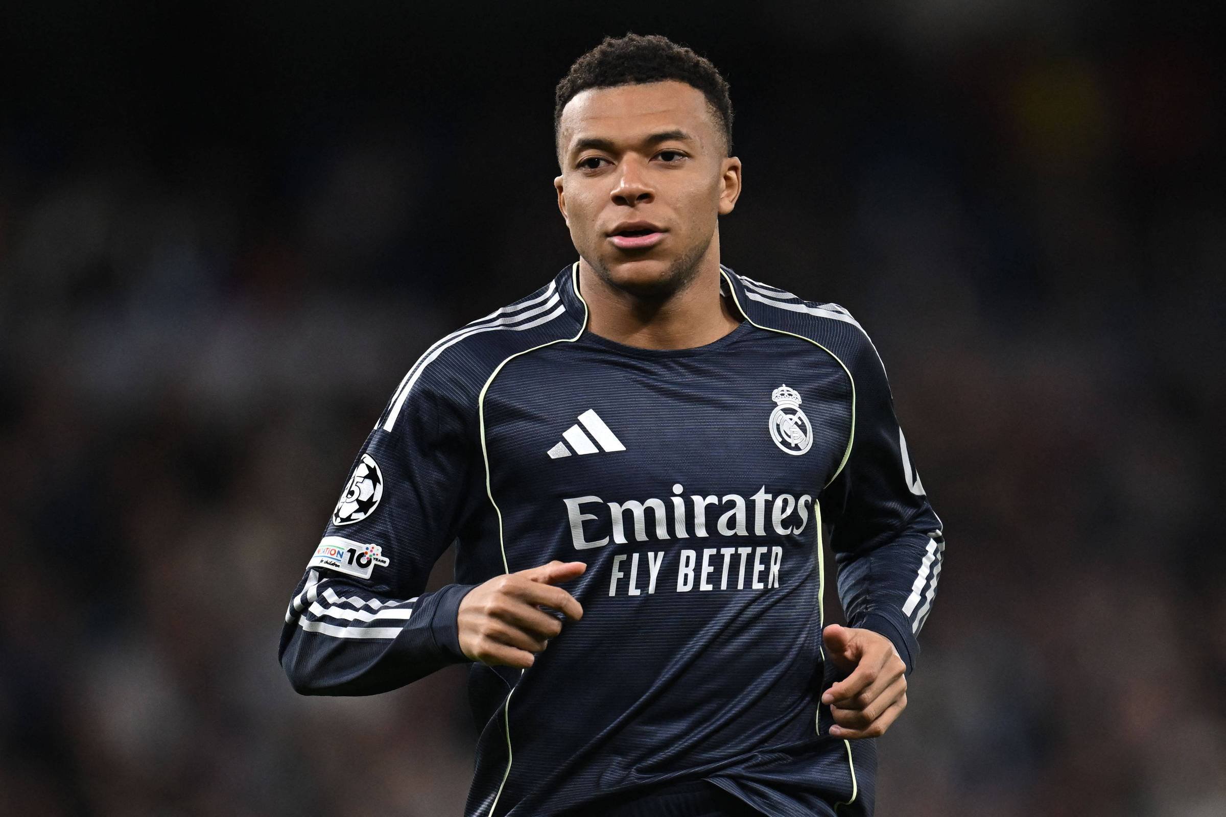 Jogador do Real Madrid com uniforme azul escuro corre em campo durante partida. Logo do clube e patrocinador visíveis na camisa.