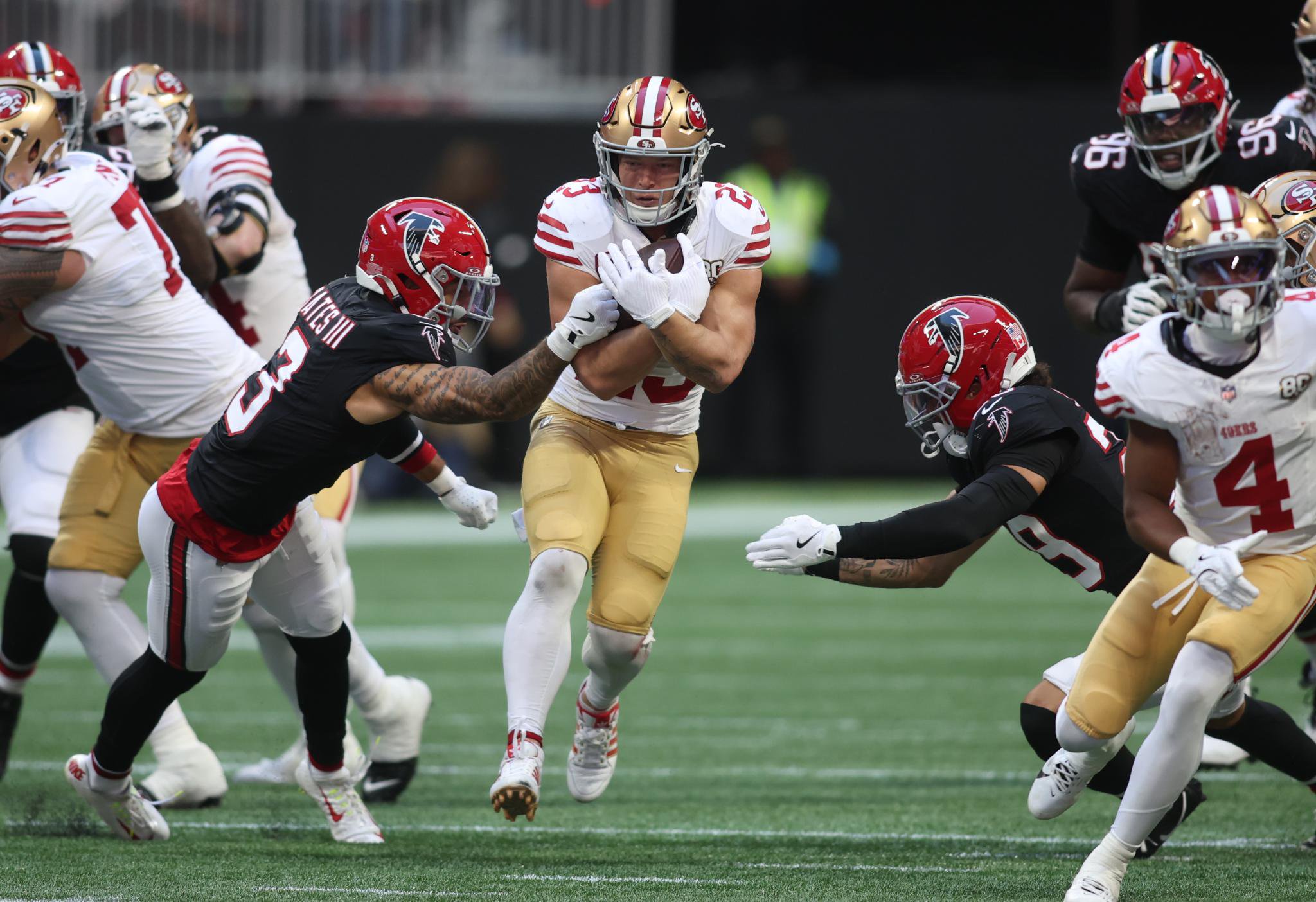 San Francisco 49ers running back Christian McCaffrey runs with the ball as Atlanta Falcons safety Jessie Bates III and cornerback Mike Ford Jr. defend during a game.