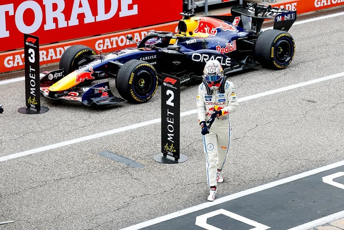 Max Verstappen walking past his Red Bull F1 car in Austin, with P2 and P3 podium markers nearby