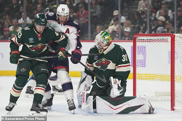 Minnesota Wild goaltender Jesper Wallstedt (30) and defenseman Quinn Hughes (43) defend against a shot as Columbus Blue Jackets center Sean Monahan (23) pressures them during the first period of an NHL hockey game, Sunday, Oct. 18, 2026, in St. Paul, Minn. (AP Photo/Abbie Parr)
