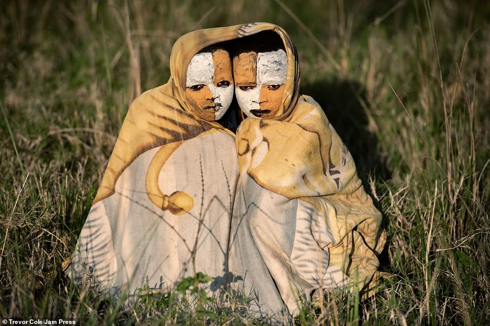Two children are photographed posing with their orange and white face paint as they huddle together in Ethiopia's Omo Valley