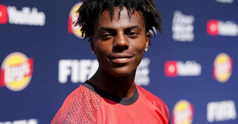 IShowSpeed in a red "YouTube FIFA Creator" shirt stands in front of a backdrop with logos, including YouTube and FIFA.