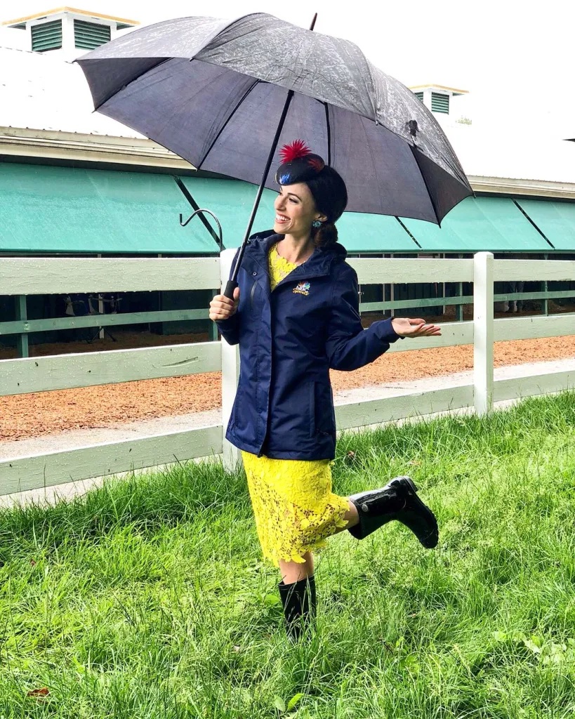 NBC Sports reporter Britney Eurton holds an umbrella in the rain at a racetrack.