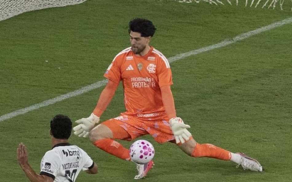 Goleiro de uniforme laranja defende chute em Flamengo x Atlético Mineiro, enquanto atacante branco avança.