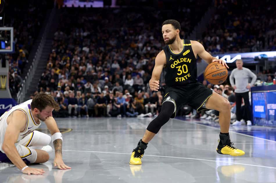 Jogador do Golden State, nº30, driblando a bola; adversário dos Lakers fica no chão durante jogo da NBA