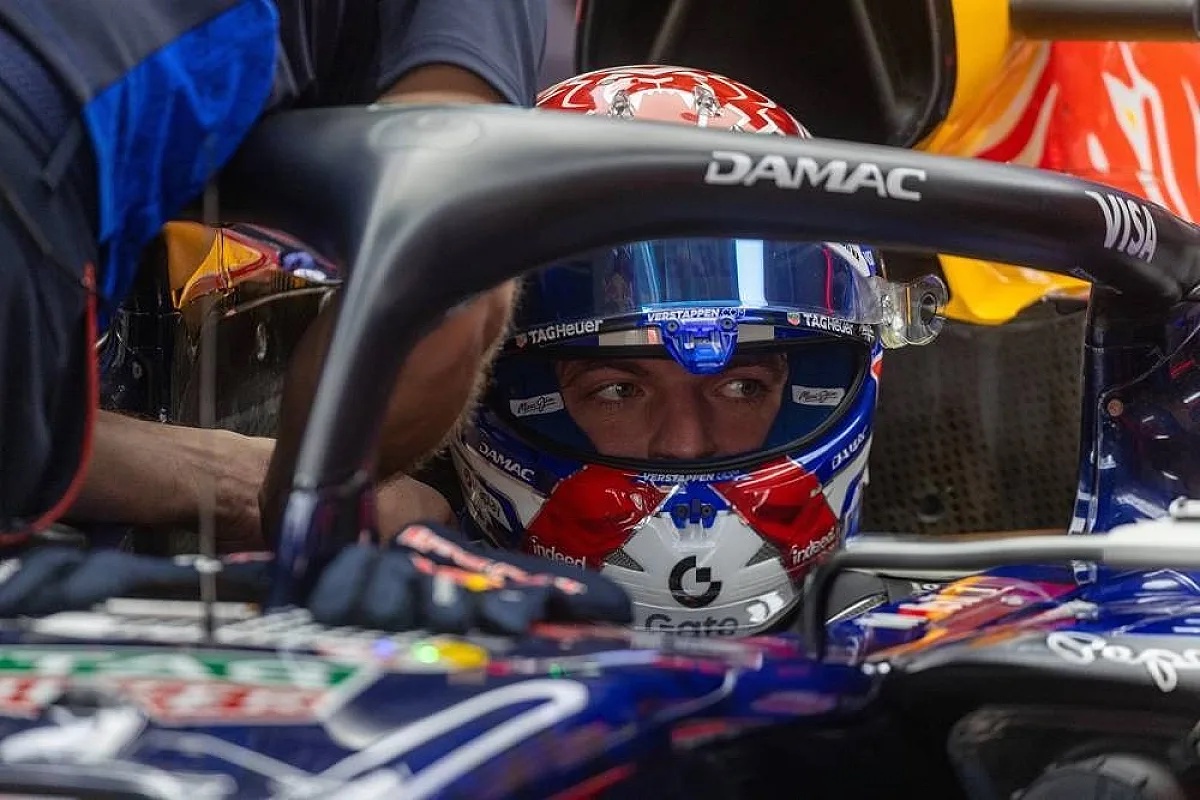 Driver in a dark blue Red Bull F1 car with a DAMAC halo, wearing a helmet with Verstappen name and Red Bull livery in the pit lane