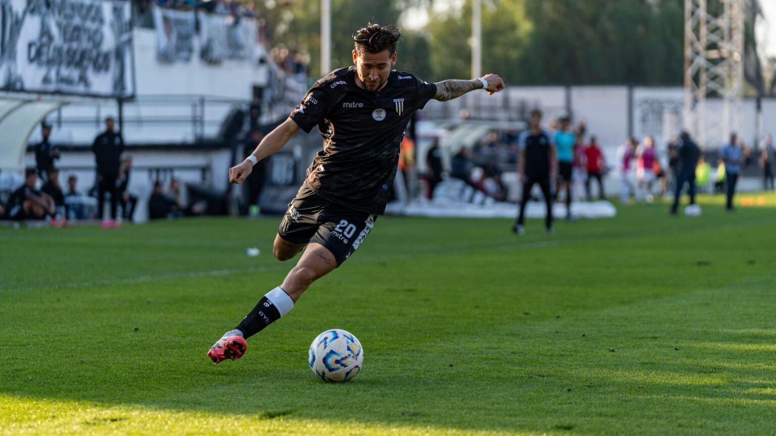 Footballer in a black and white kit about to strike the ball first time during a match
