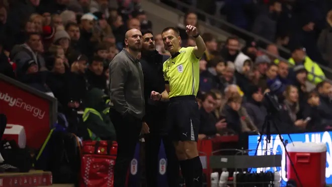 Referee Michael Salisbury talks with Matt Lawlor, Manager of Fleetwood Town, as the game is paused due to a drone being spotted above the pitch