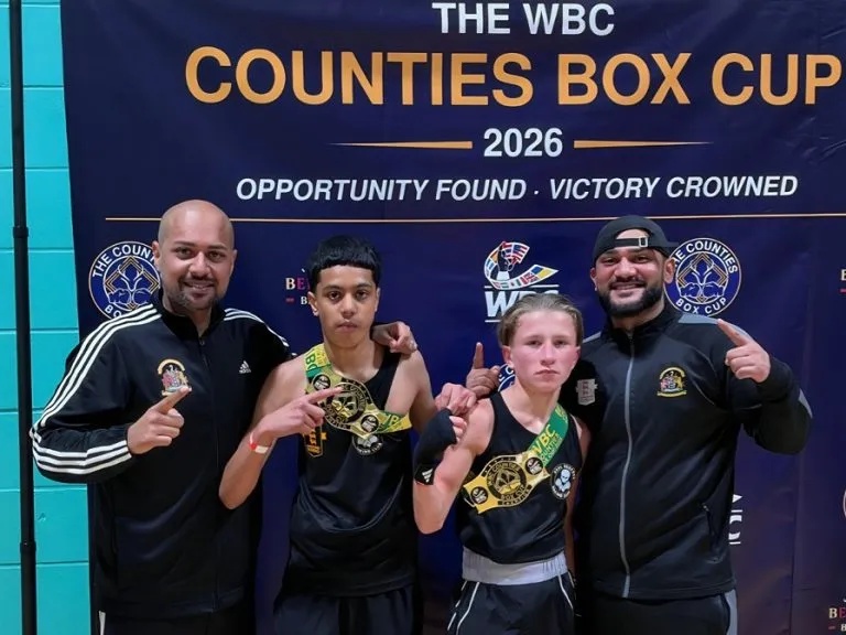 Real Bedford boxers, Musa Khan and Jeremiah Fletcher with two of their coaches in front of the WBC Counties Box Cup sign