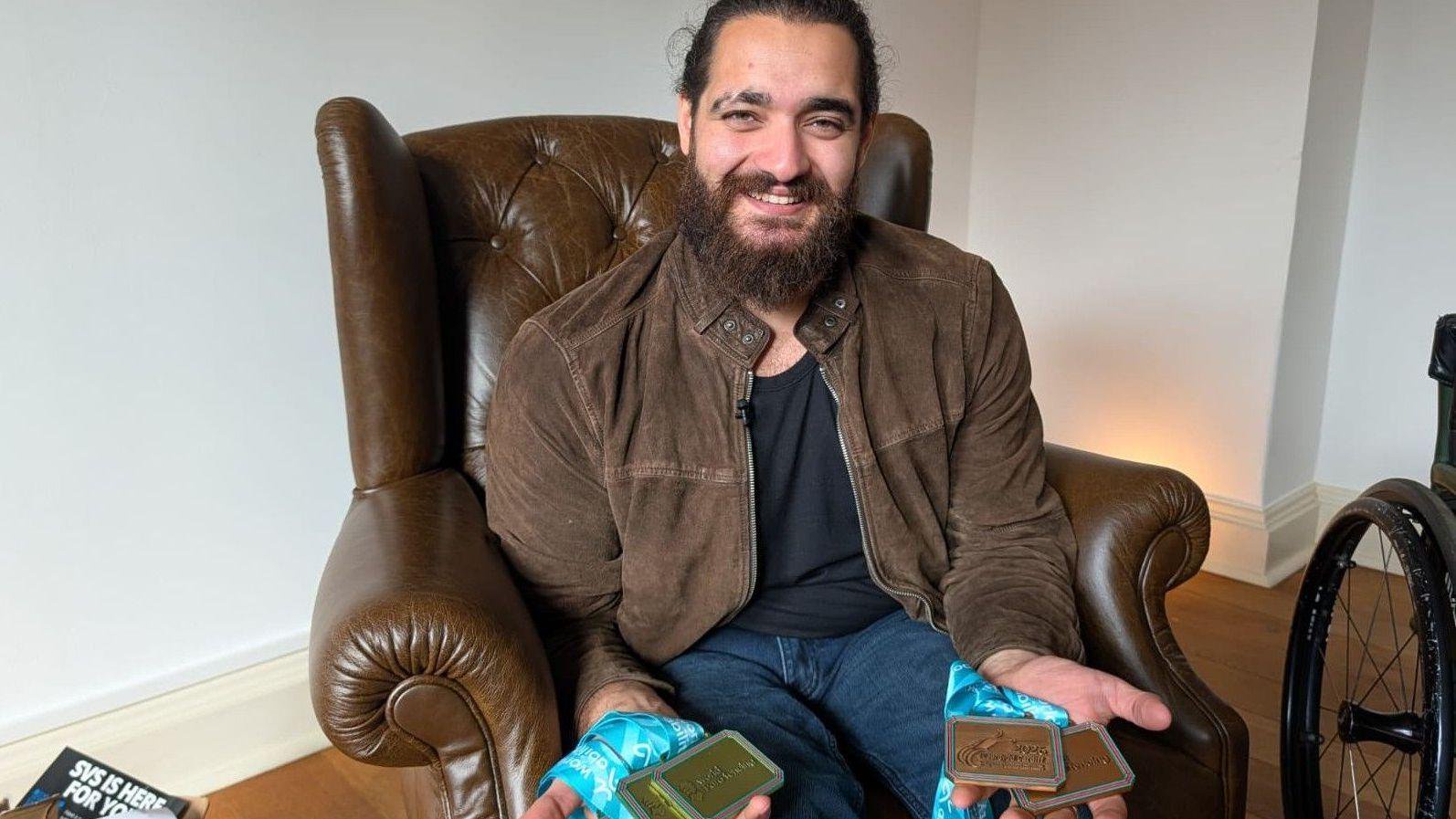 Dimitri Coutya sat in an armchair holding his European Para-fencing medals in his hands