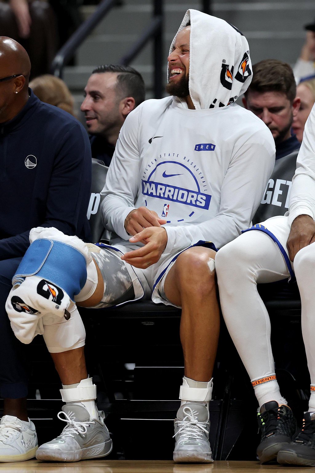 Stephen Curry of the Golden State Warriors watches from the bench with a towel over his head during an NBA basketball game.