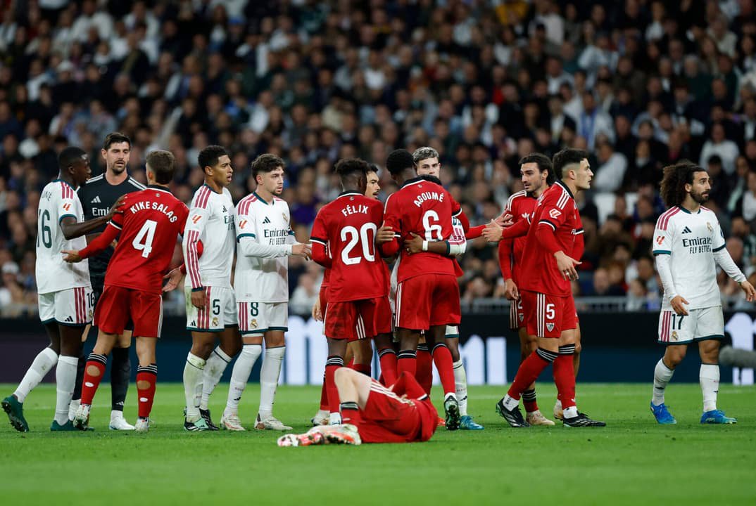 Jogadores conversam enquanto o atacante espanhol do Sevilla, camisa 10 Gerard Peque, está caído no chão durante a partida do Campeonato Espanhol entre Real Madrid CF e Sevilla FC, no estádio Santiago Bernabéu, em Madri, em 18 de outubro de 2026. (Foto: Oscar Del Pozo / AFP)