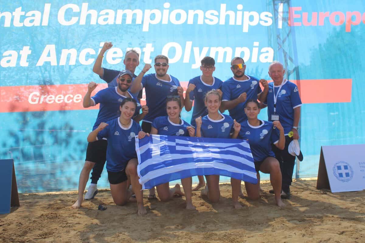 Greek AirBadminton team holding a Greek flag on a sand court