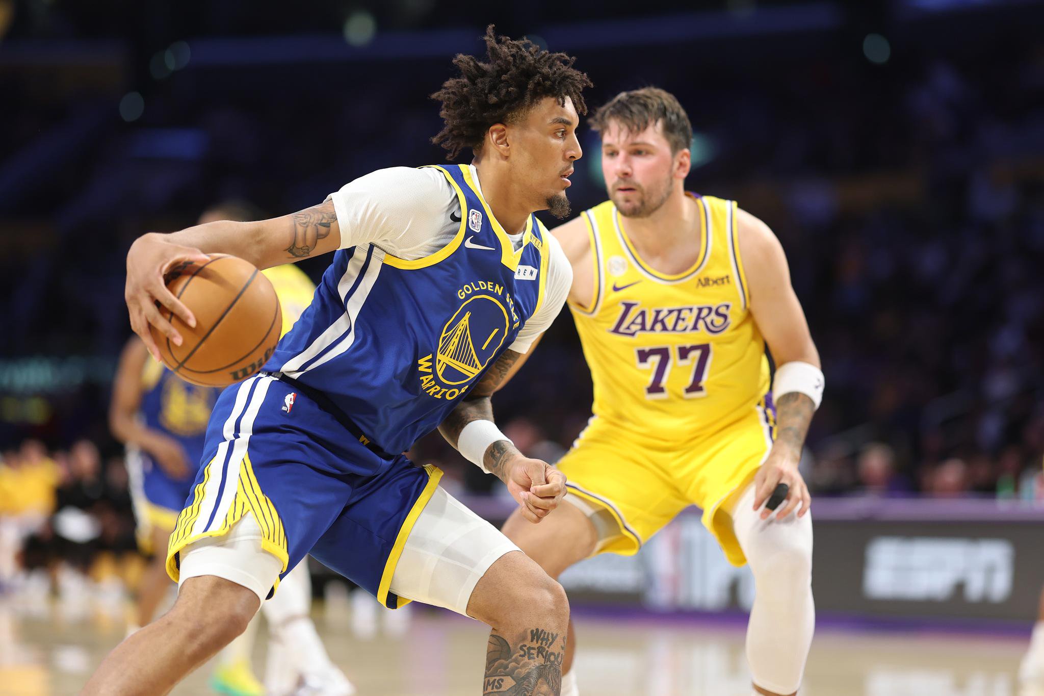 A Golden State Warriors player dribbles the basketball while being defended by a Los Angeles Lakers player.