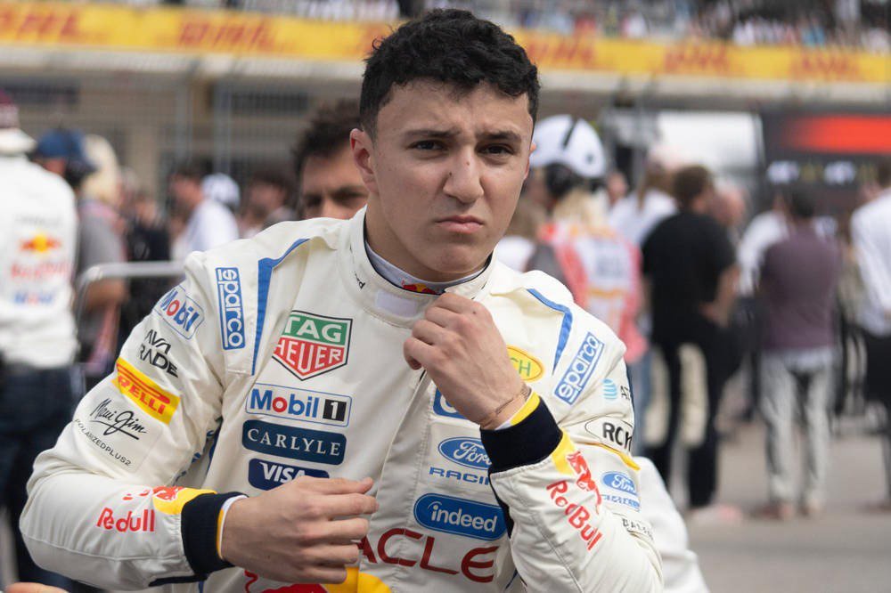 Racing driver in white Red Bull-branded suit with Tag Heuer, Mobil 1, Ford Racing logos on the grid at the US Grand Prix in Austin