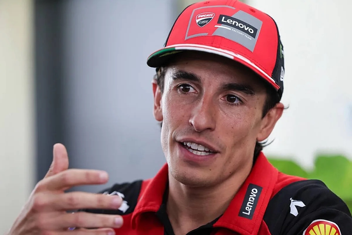 A rider in a red Ducati Lenovo Factory Team cap and shirt speaks to reporters in the MotoGP paddock, gesturing with one hand.
