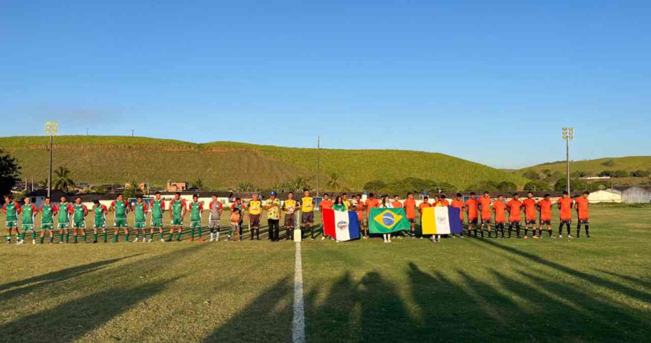 Equipes de futebol e arbitragem alinhadas no gramado durante a cerimônia de abertura do Campeonato Lajense de Futebol.
