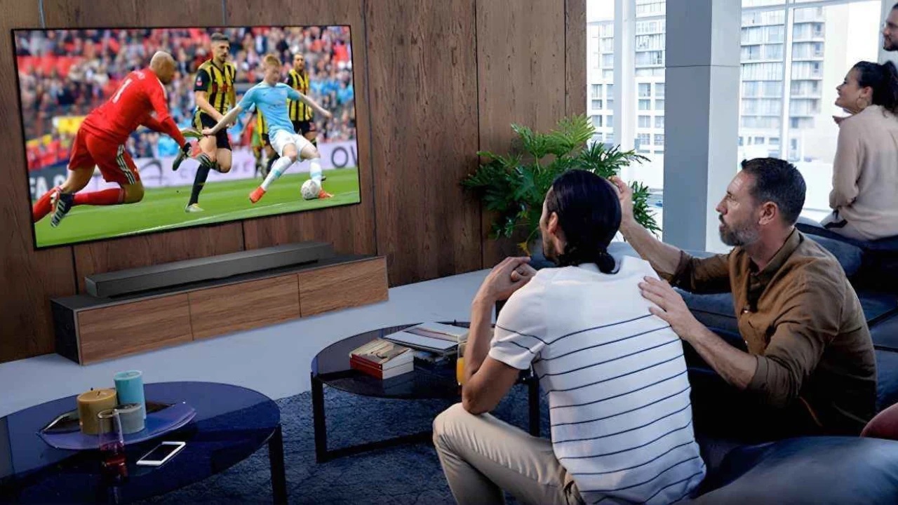Grupo de amigos sentados em um sofá assistindo uma partida de futebol na TV