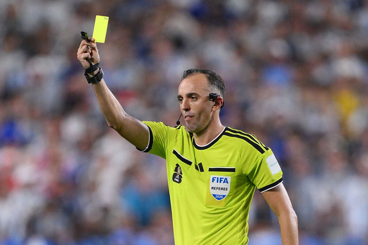 Soccer referee in a lime green jersey holds up a yellow card, signaling a foul during a match.