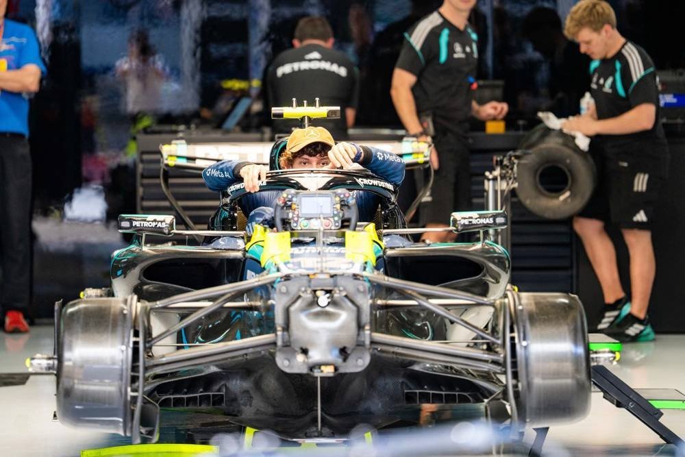 A driver in a Mercedes F1 car in the garage, with Petronas-branded team staff behind, illustrating the F1 car weight article