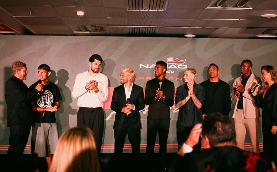 Grupo no palco durante leilão, alguns segurando microfones; fundo com logotipo e público ao redor.