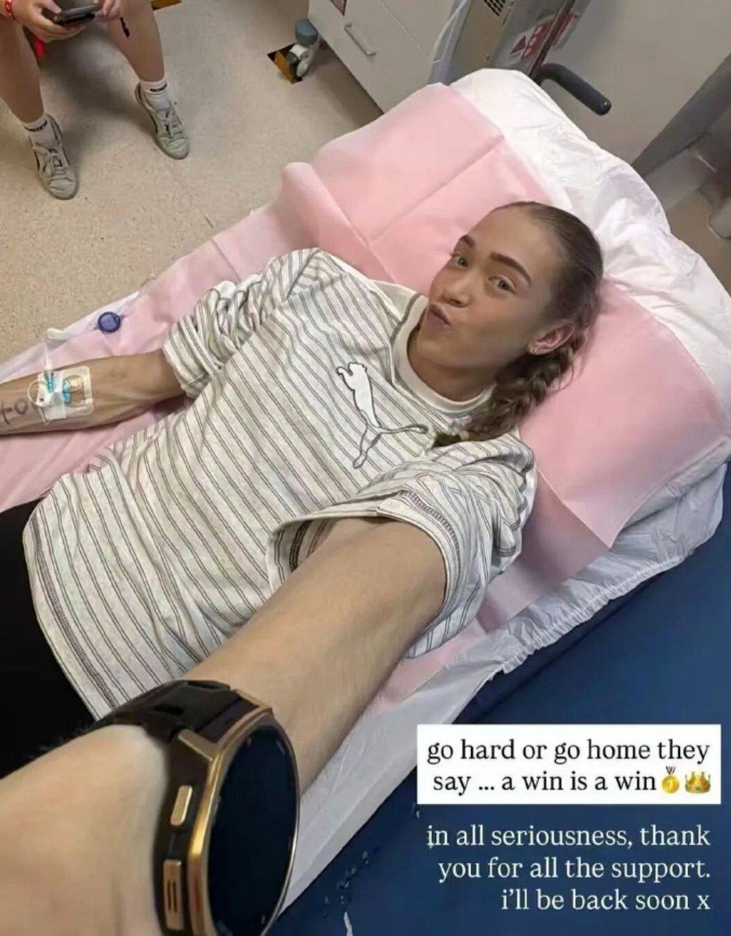 HYROX athlete Joanna Wietrzyk lies on a medical bed taking a selfie, with an IV line in her arm.