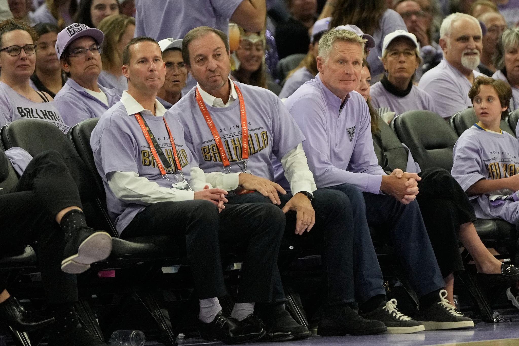 Brandon Schneider, Joe Lacob, and Steve Kerr seated courtside.
